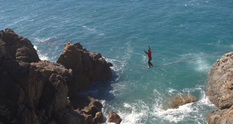 A young man balancing on a rope above the water