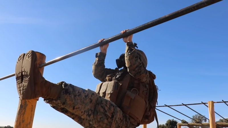 A Soldier Performs a High-Bar Obstacle Course Exercise During a Tactical Military Training Session Under a Clear Blue Sky