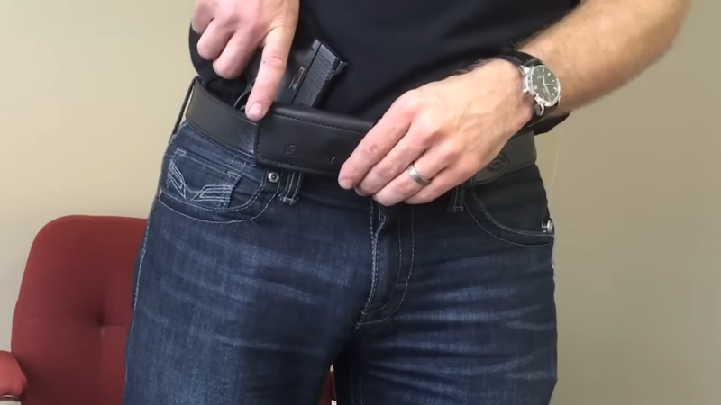 A Close-Up of A Person Demonstrating the Concealed Carry of A Firearm Using a Belt Holster