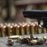 close-up of a handgun on a wooden surface with scattered ammunition in the foreground. The image emphasizes the importance of firearm maintenance