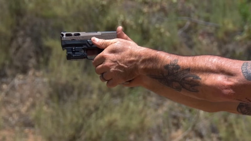 A Person Is Holding a Pistol with Both Hands in A Firm Grip During Target Practice Outdoors