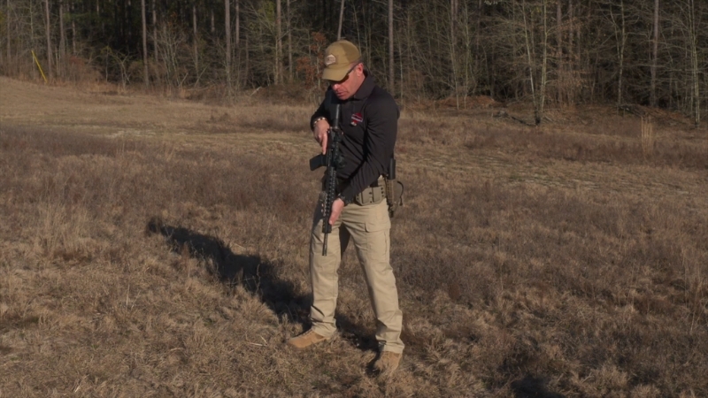 A Man Standing in An Open Field Is Handling a Rifle, Keeping the Muzzle Pointed Down