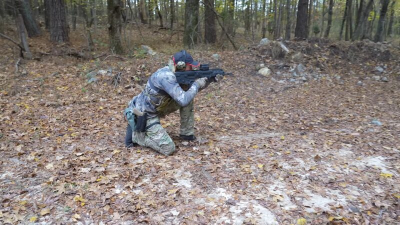 Person Wearing Military Fashion, Including Camouflage and Tactical Gear, Takes a Kneeling Position While Aiming at A Gun Range