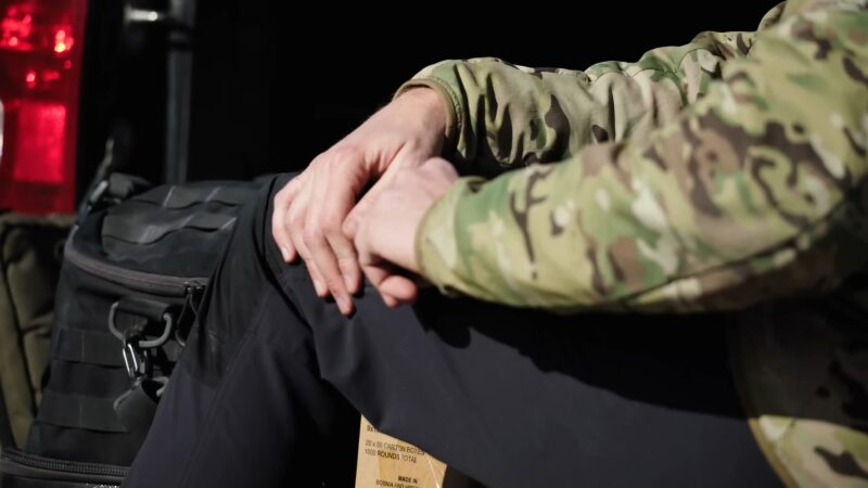 Man in A Camouflage Jacket Sits with Hands Resting on His Knees