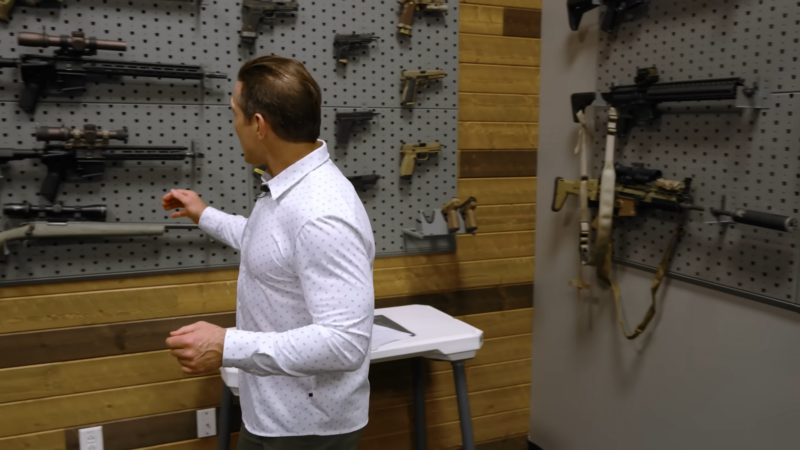 A Man in A Showroom Examining Various Firearms, Including Pistols and Rifles, Displayed on A Wall