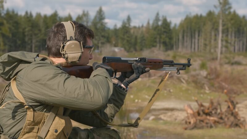 A Man Outdoors Aiming a Rifle in A Shooting Stance, Demonstrating the Precision and Long-Range Capabilities of Rifles