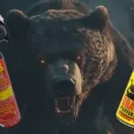 A fierce bear in the background with glowing eyes, flanked by a Sabre Wild Max bear spray canister on the left and a Dragon pepper spray canister on the right