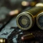 Close-up view of two shotgun shell bases resting on a wooden surface, with scattered bullets in the background