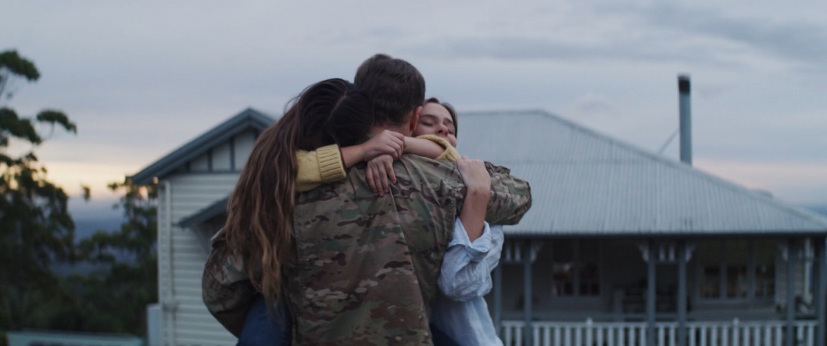 Family embracing a military service member in uniform outdoors