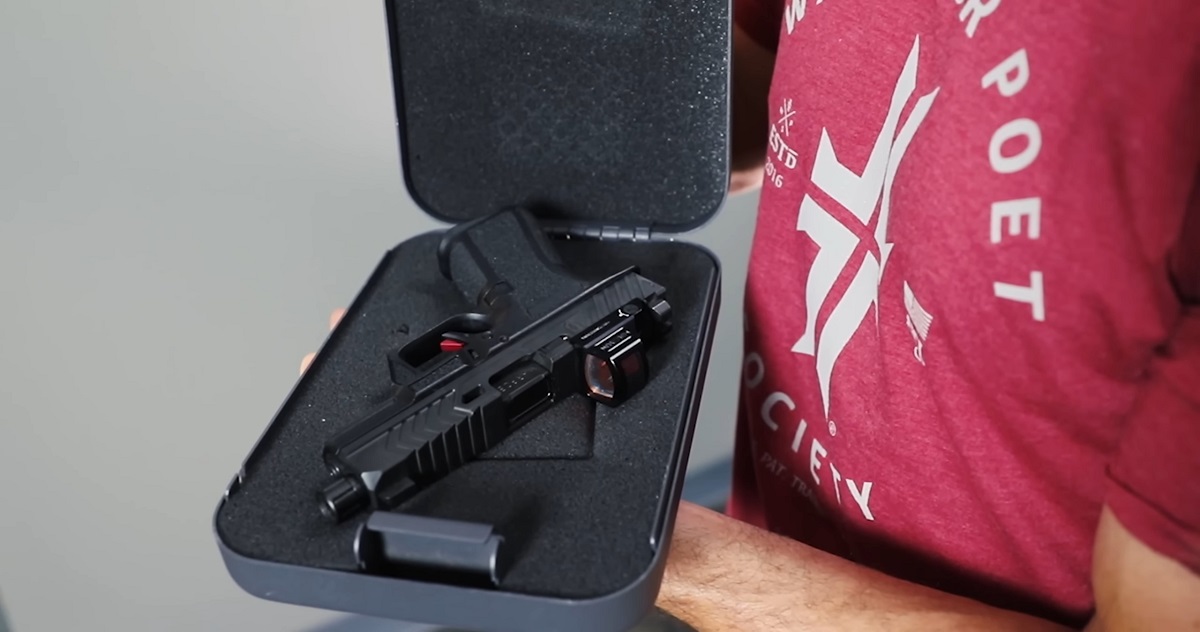 A person wearing a red shirt holding an open gun case with a customized handgun inside, equipped with a red dot sight