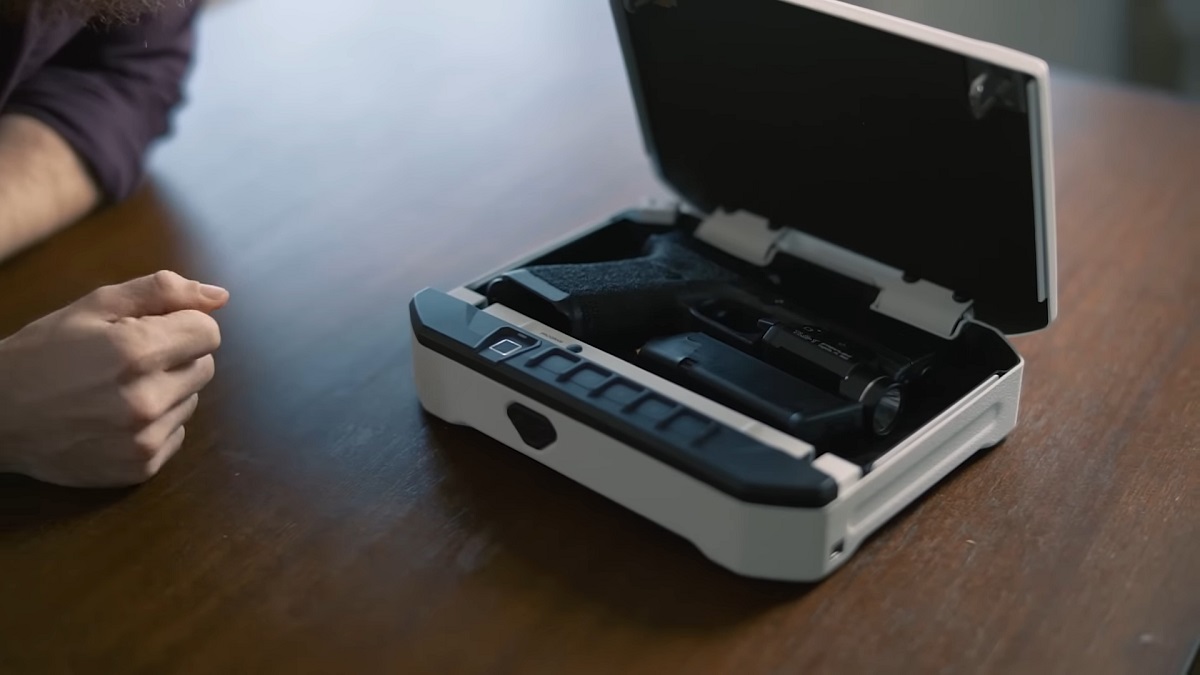 A biometric gun safe on a wooden table, containing a secured black handgun with an attached flashlight