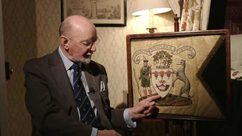 The Image Shows a Man Pointing to A Heraldic Coat of Arms, Illustrating the Concept of Ancient Symbolism in Heraldry